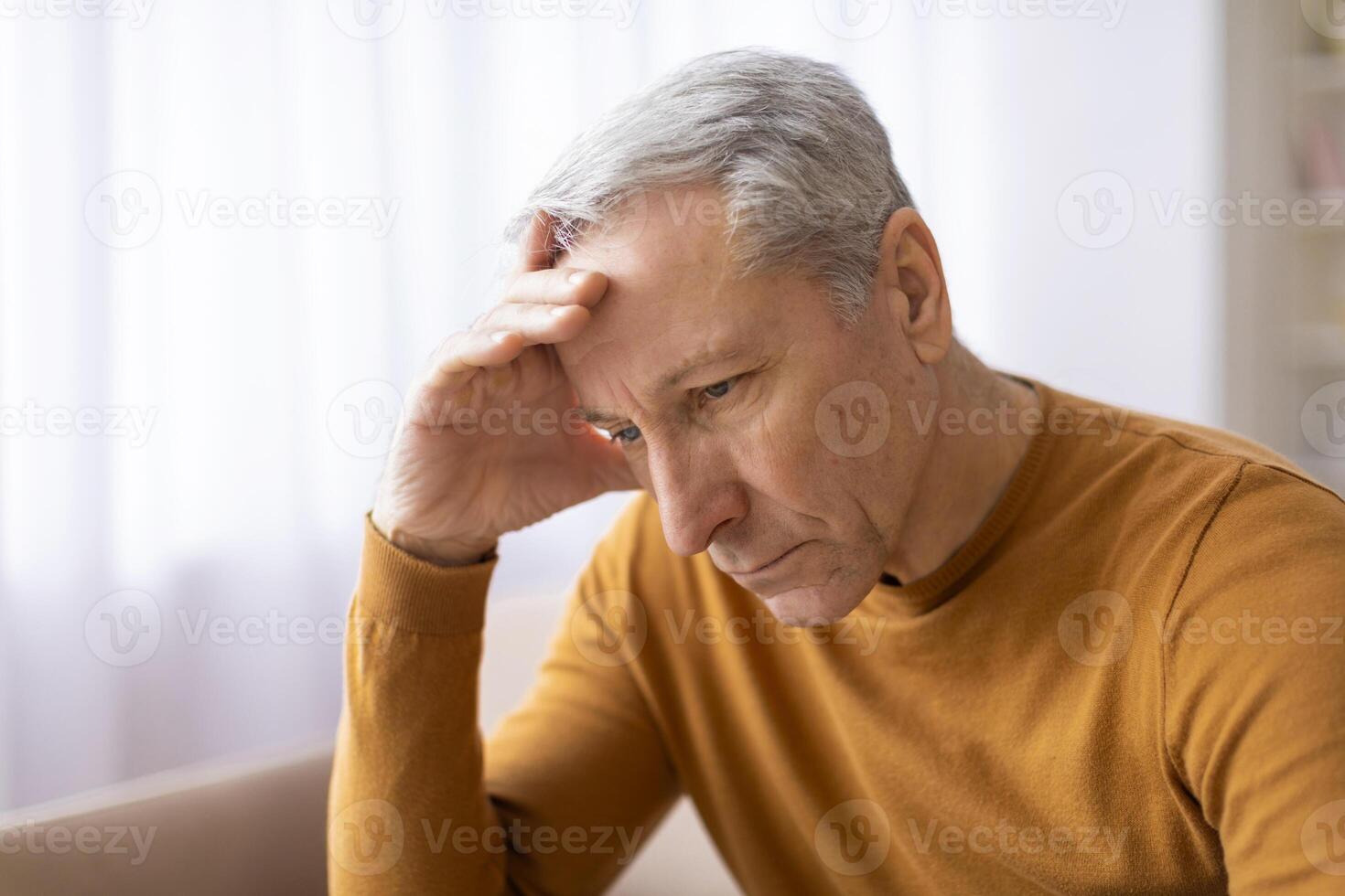 Aged man holds forehead in an upset manner photo