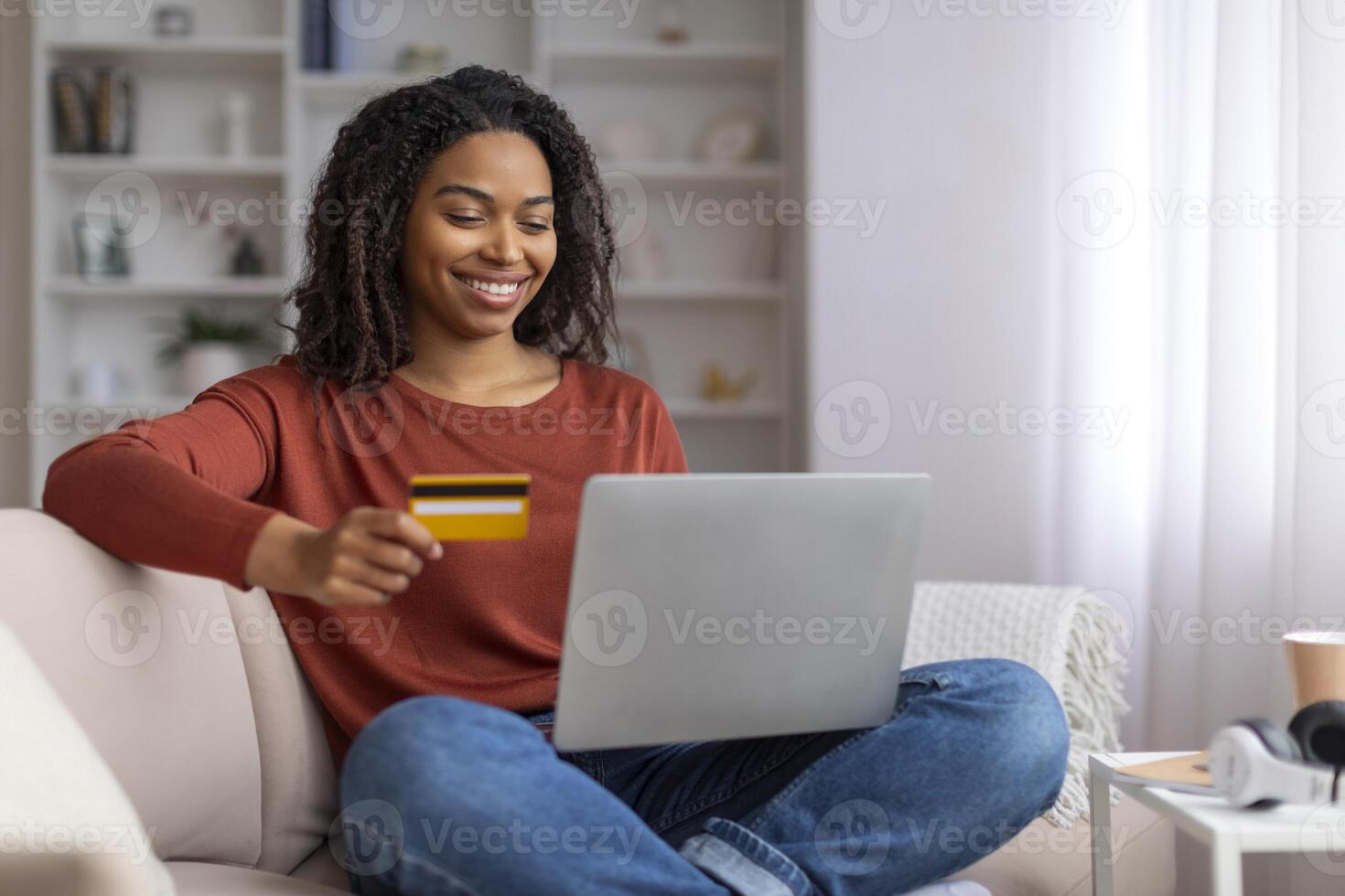 alegre joven negro mujer utilizando crédito tarjeta para en línea compras en ordenador portátil foto