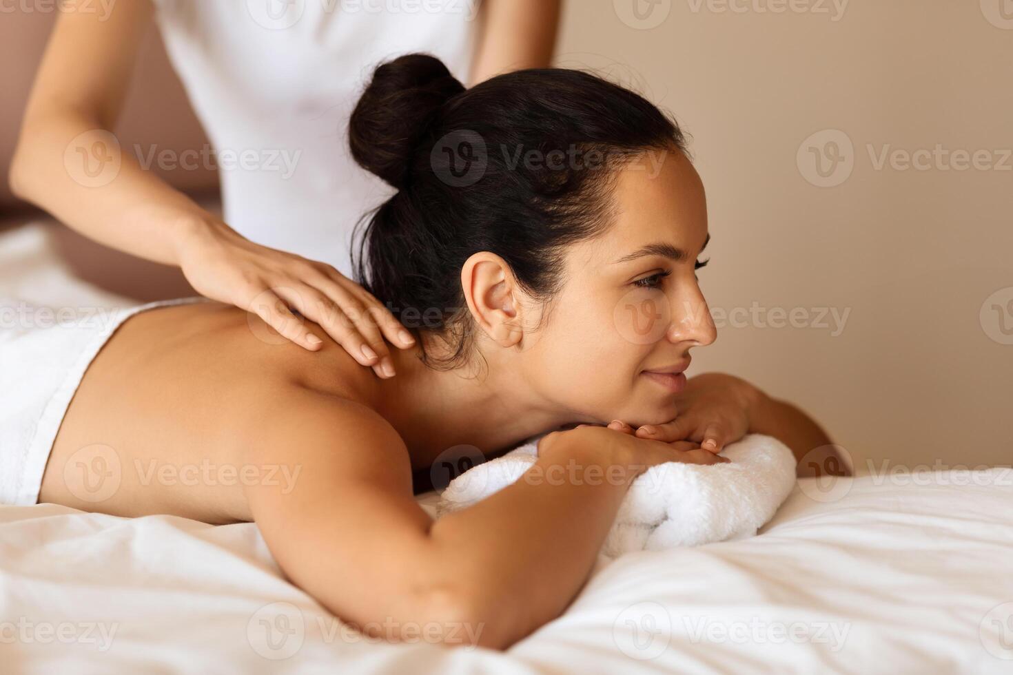 Attractive millennial woman with brunette hair receives back massage indoor photo