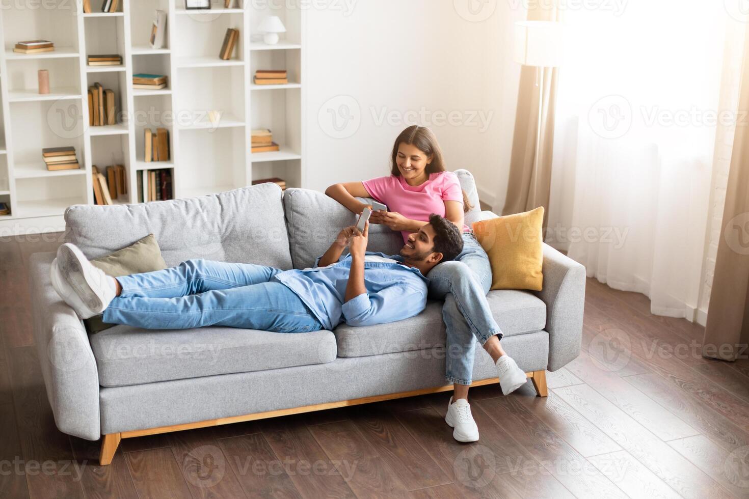 Relaxed indian couple on couch with phone enjoying home time photo