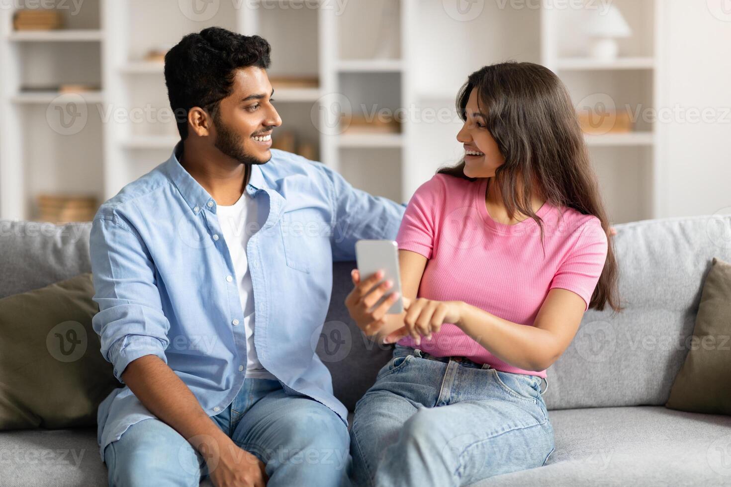 Hindu couple on couch sharing phone, both smiling photo