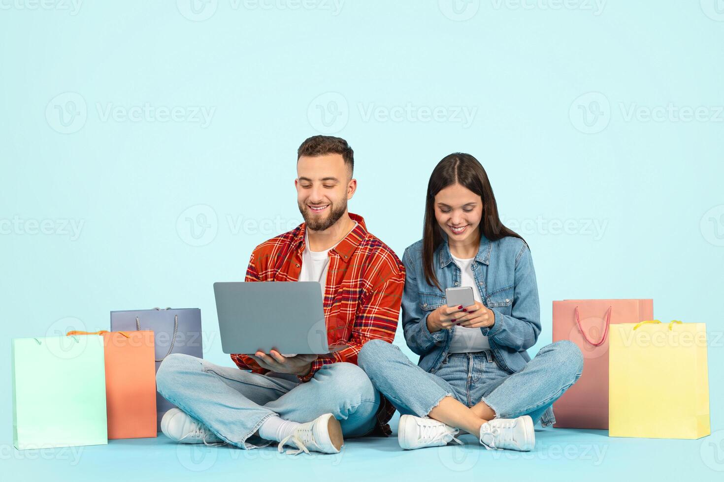 couple with bags making purchases via laptop and smartphone, studio photo