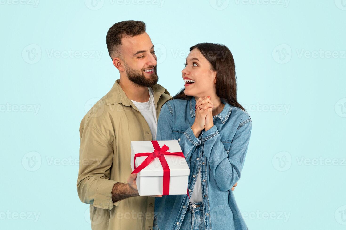 Cheerful caucasian man gives wrapped present box congratulating wife, studio photo