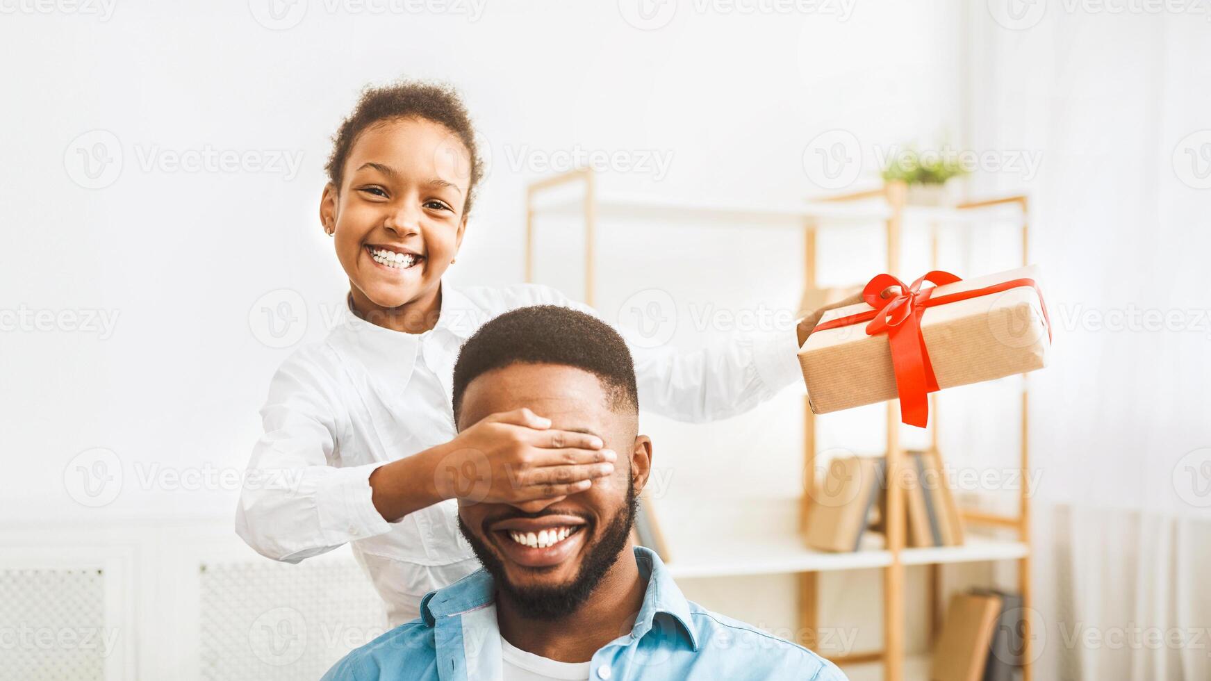 Cute afro girl closing father's eyes and making surprise photo