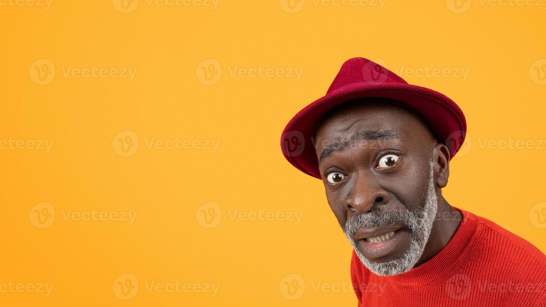 Surprised senior black man in red hat and sweater with a comically raised eyebrow photo