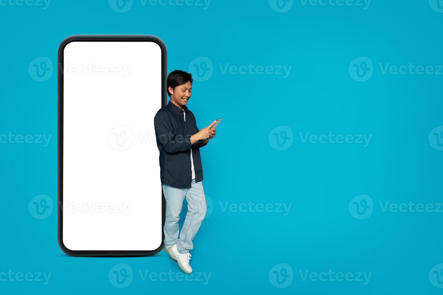 Happy Asian man standing and using a phone with a huge blank smartphone screen photo