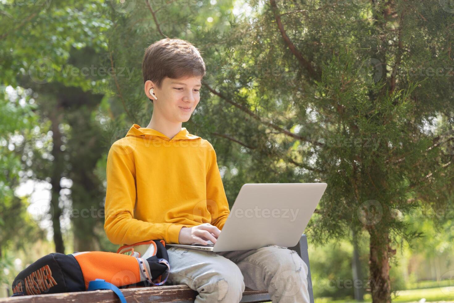Smiling teenager boy working on laptop. Holding and using a laptop for networking on a sunny spring day, outdoors. photo