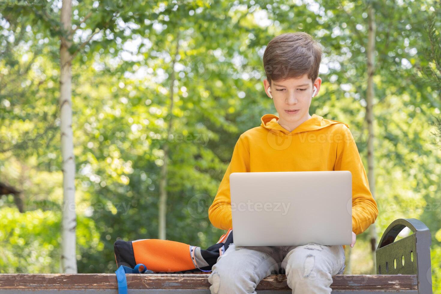 Thoughtful teenager boy working on laptop. Holding and using a laptop for networking on a sunny spring day, outdoors. photo