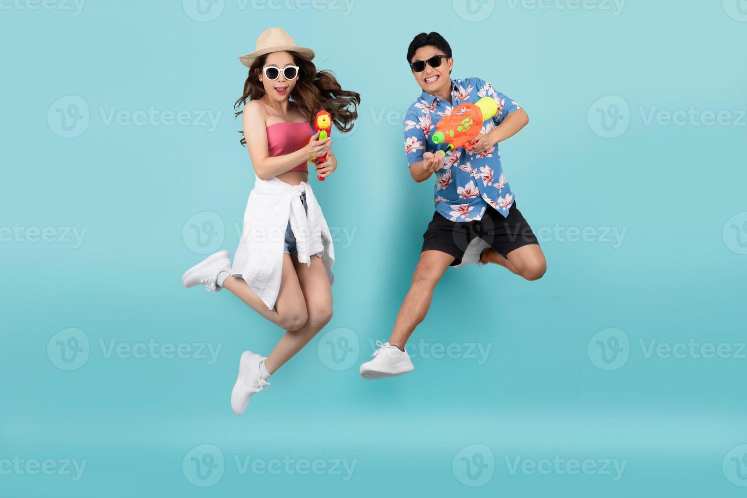 Happy Asian couple jumping and using water guns on blue background. Songkran Festival in Thailand photo