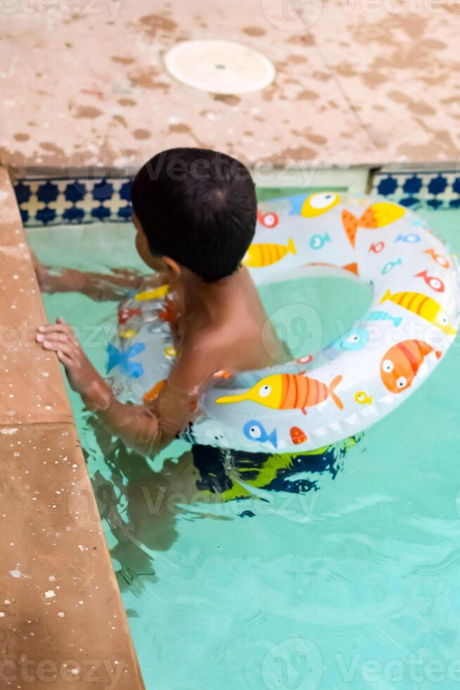 contento indio chico nadando en un piscina, niño vistiendo nadando disfraz a lo largo con aire tubo durante caliente verano vacaciones, niños chico en grande nadando piscina. foto