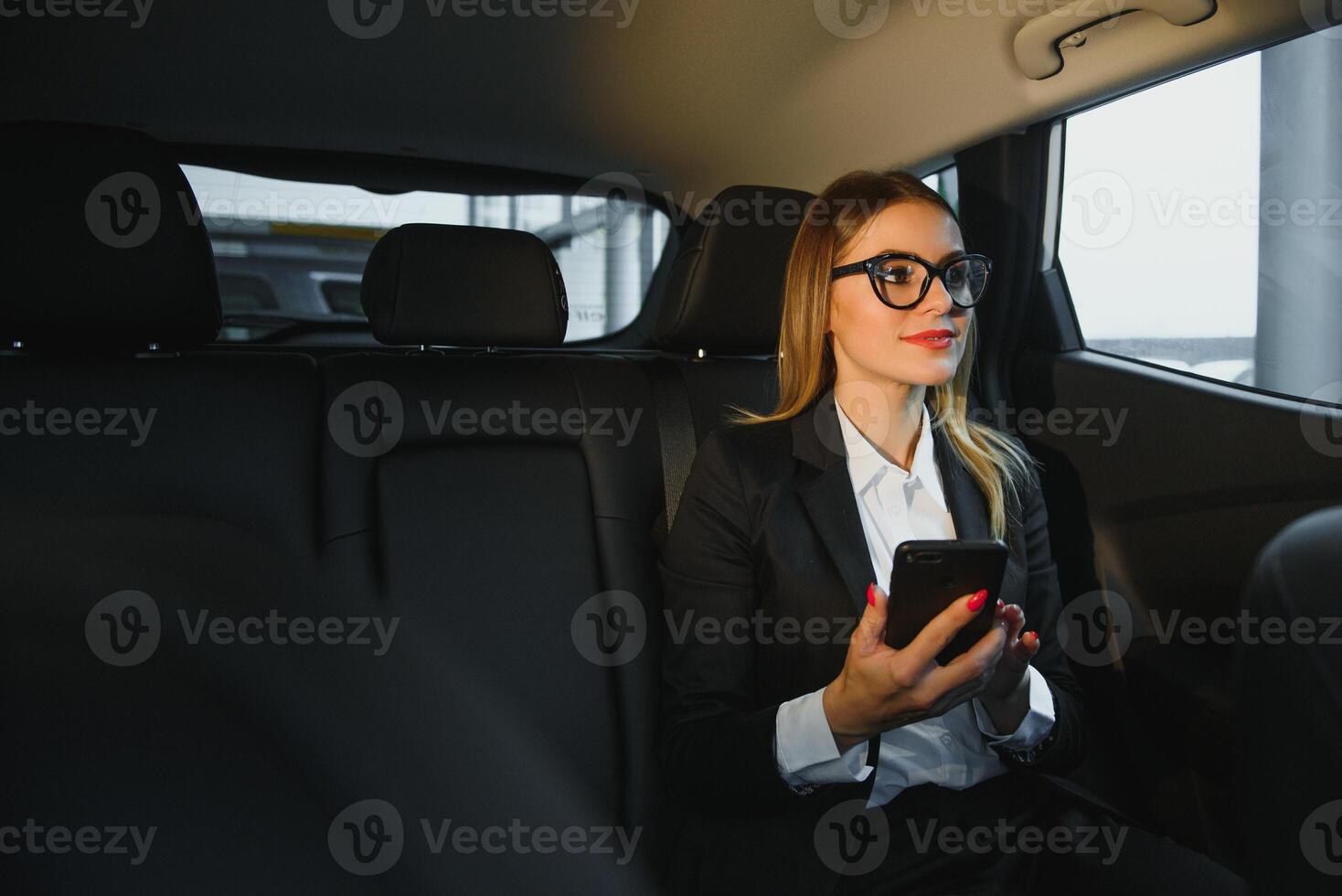 Some sort of interesting information. Smart businesswoman sits at backseat of the luxury car with black interior. photo