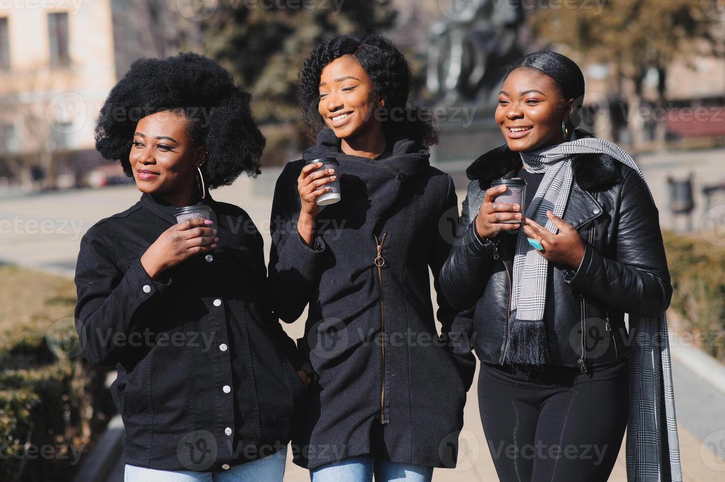 three stylish african american girls drinking coffee on the street and having fun photo