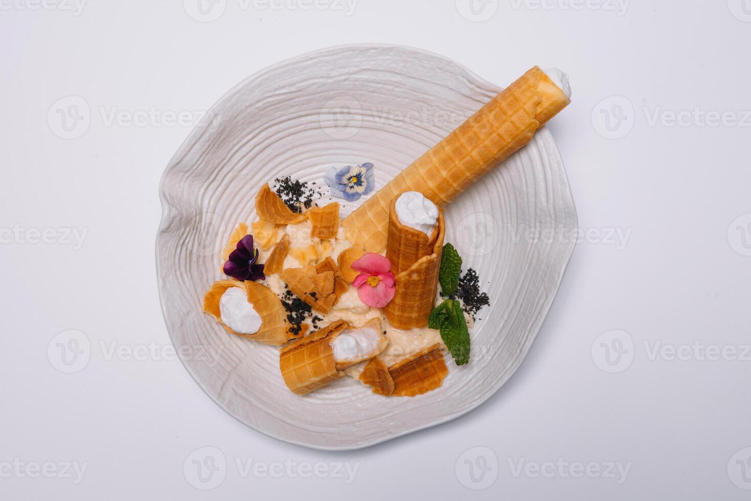 Sweet dessert. Wafer tubules with a delicate protein cream and a small sieve with powdered sugar on a white round tray on a white background. photo