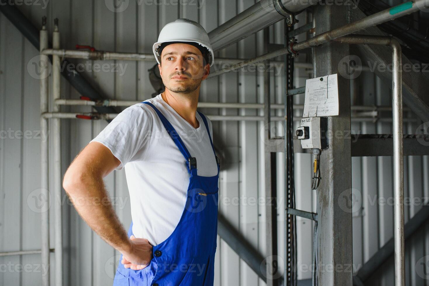 Smiling and happy employee. Industrial worker indoors in factory. Young technician with white hard hat. photo