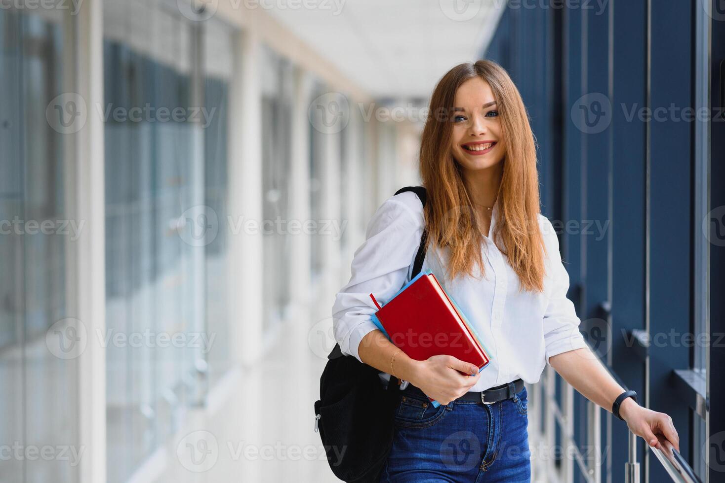 Positivity beautiful girl smiling at camera, standing on corridor with notes as backpack, going to lesson. Happy brunette female student studying in luxury university. photo