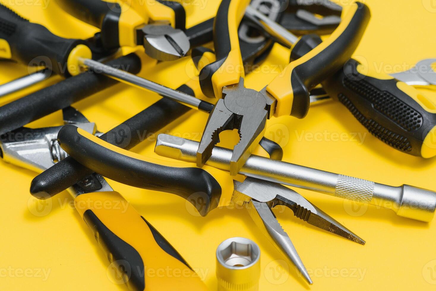 Yellow and black handy tools pilers and screwdriver isolated on yellow background. photo