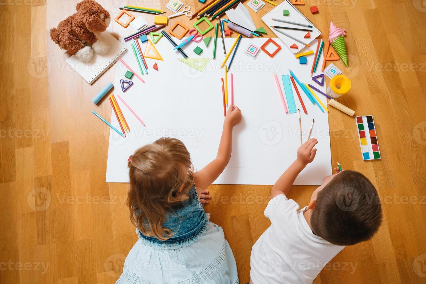 Kids drawing on floor on paper. Preschool boy and girl play on floor with educational toys - blocks, train, railroad, plane. Toys for preschool and kindergarten. Children at home or daycare. Top view. photo