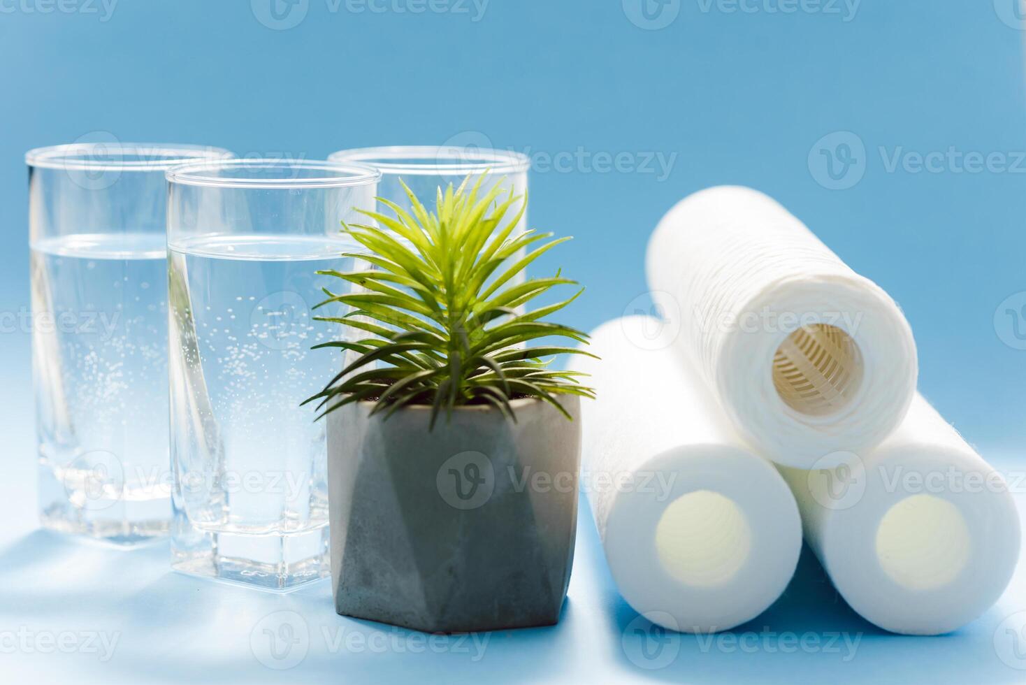 Glasses of dirty and clear water and filter cartridges to domestic water treatment systems at bright blue background. Concept of water treatment. photo