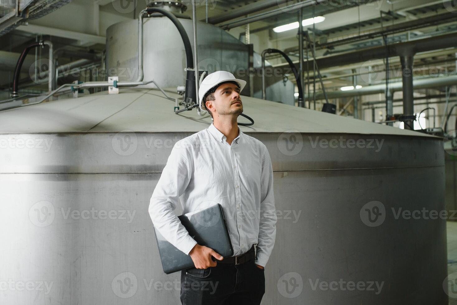 Smiling and happy employee. Industrial worker indoors in factory. Young technician with white hard hat. photo