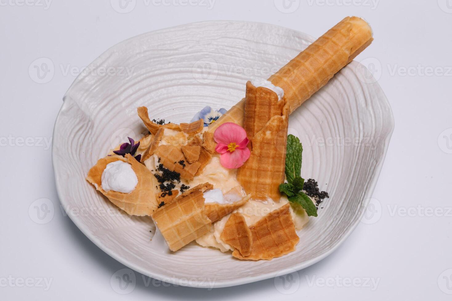Sweet dessert. Wafer tubules with a delicate protein cream and a small sieve with powdered sugar on a white round tray on a white background photo