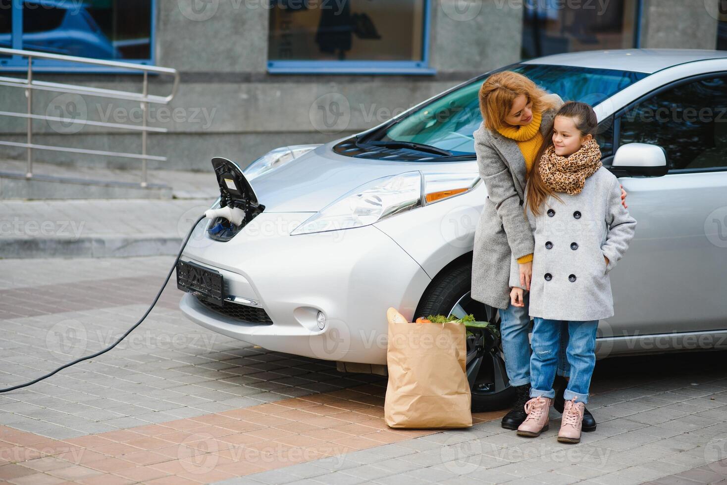 Stylish mother and daughter charge an electric car, and spend time together. photo
