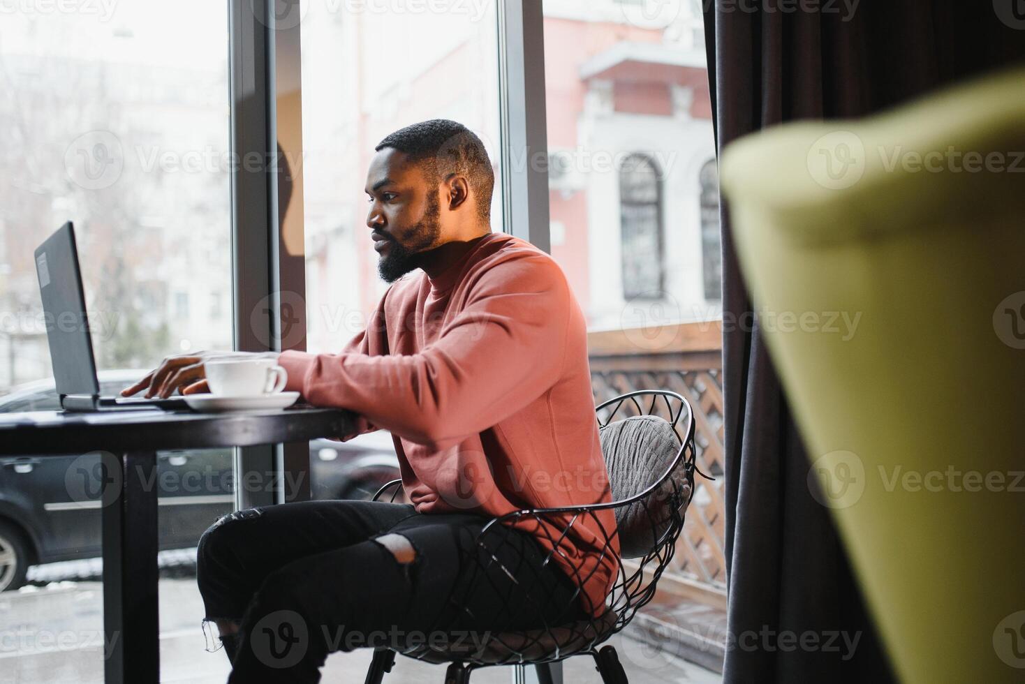 retrato de contento africano empresario sentado en un café y trabajando en ordenador portátil. foto