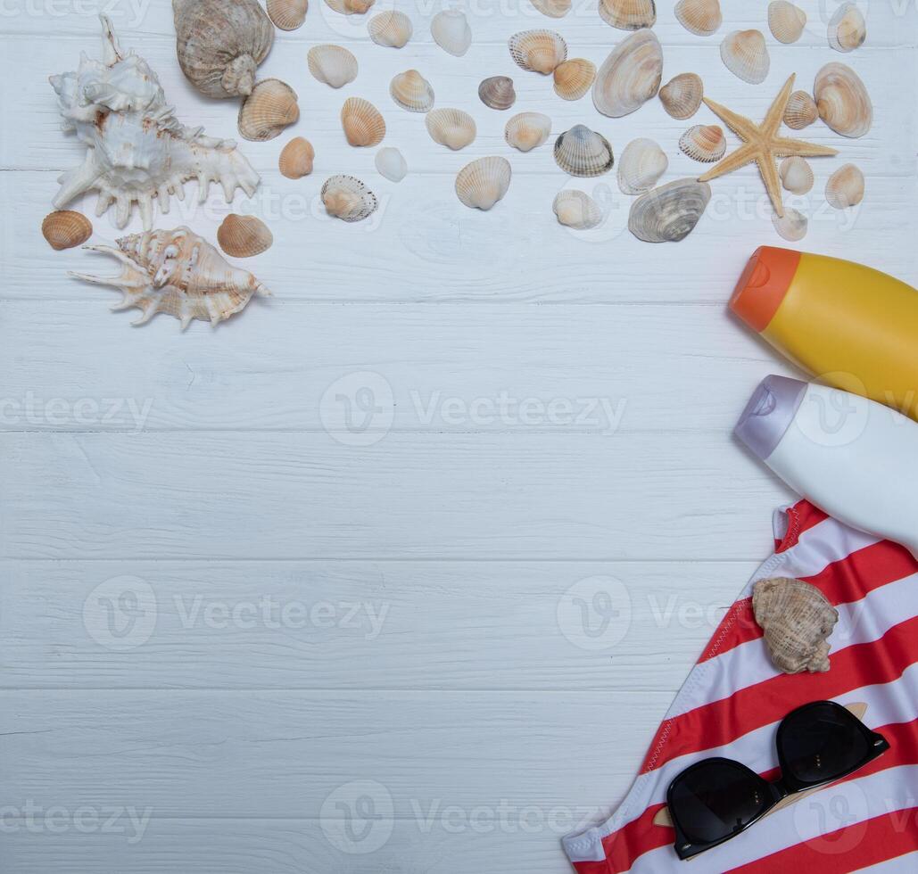 playa accesorios. toalla, chancletas, estrella de mar, barco y Gafas de sol en de madera antecedentes. parte superior ver con Copiar espacio. soleado tonificado foto