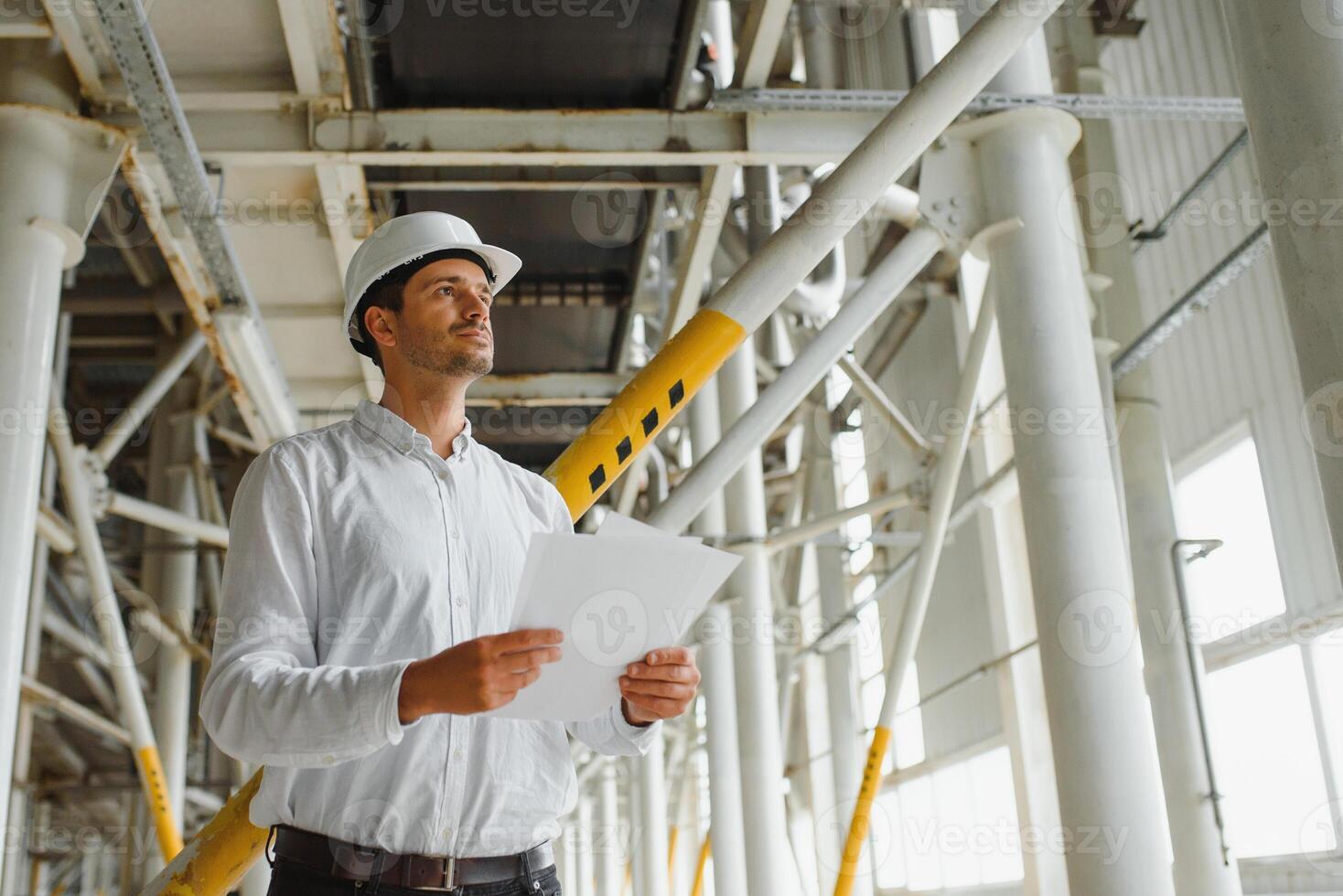 A young successful engineer with a drawing in his hands is standing in the territory of a modern factory. photo