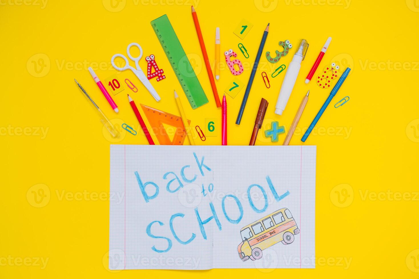 School notebook and stationery over yellow desk. Back to school abstract background. School equipment. Variety of school supplies. Flat lay photo