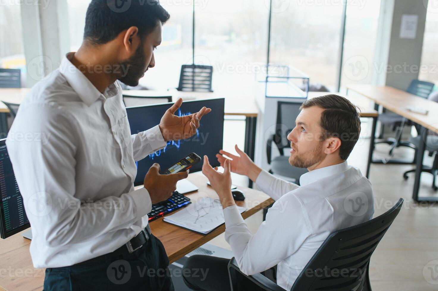 Two successful trader sitting in office and looking at screen, checking cryptocurrency information data on finance market graph, pointing on monitor photo