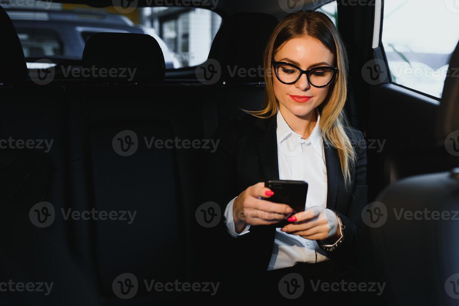 Some sort of interesting information. Smart businesswoman sits at backseat of the luxury car with black interior. photo