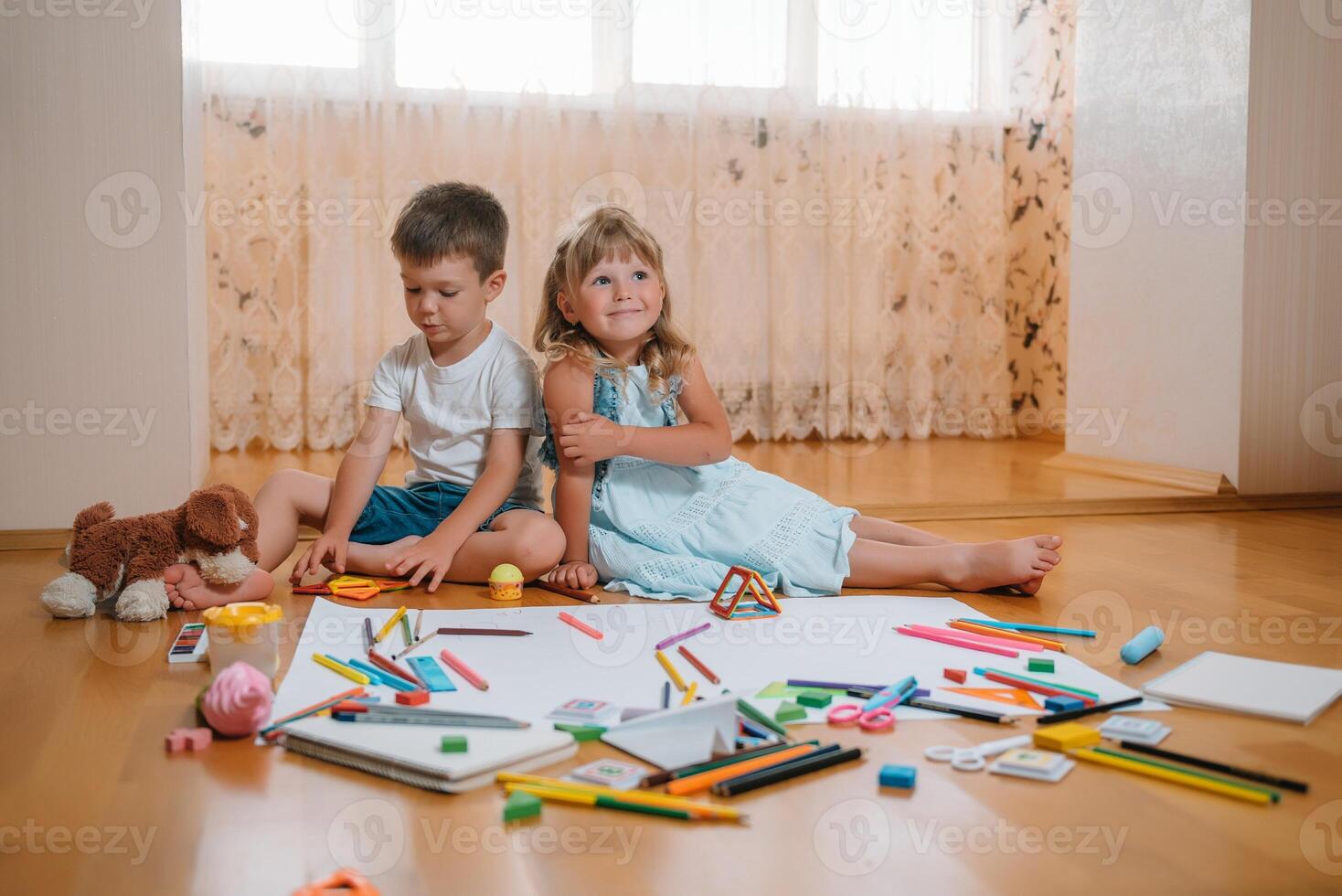 Kids drawing on floor on paper. Preschool boy and girl play on floor with educational toys - blocks, train, railroad, plane. Toys for preschool and kindergarten. Children at home or daycare photo