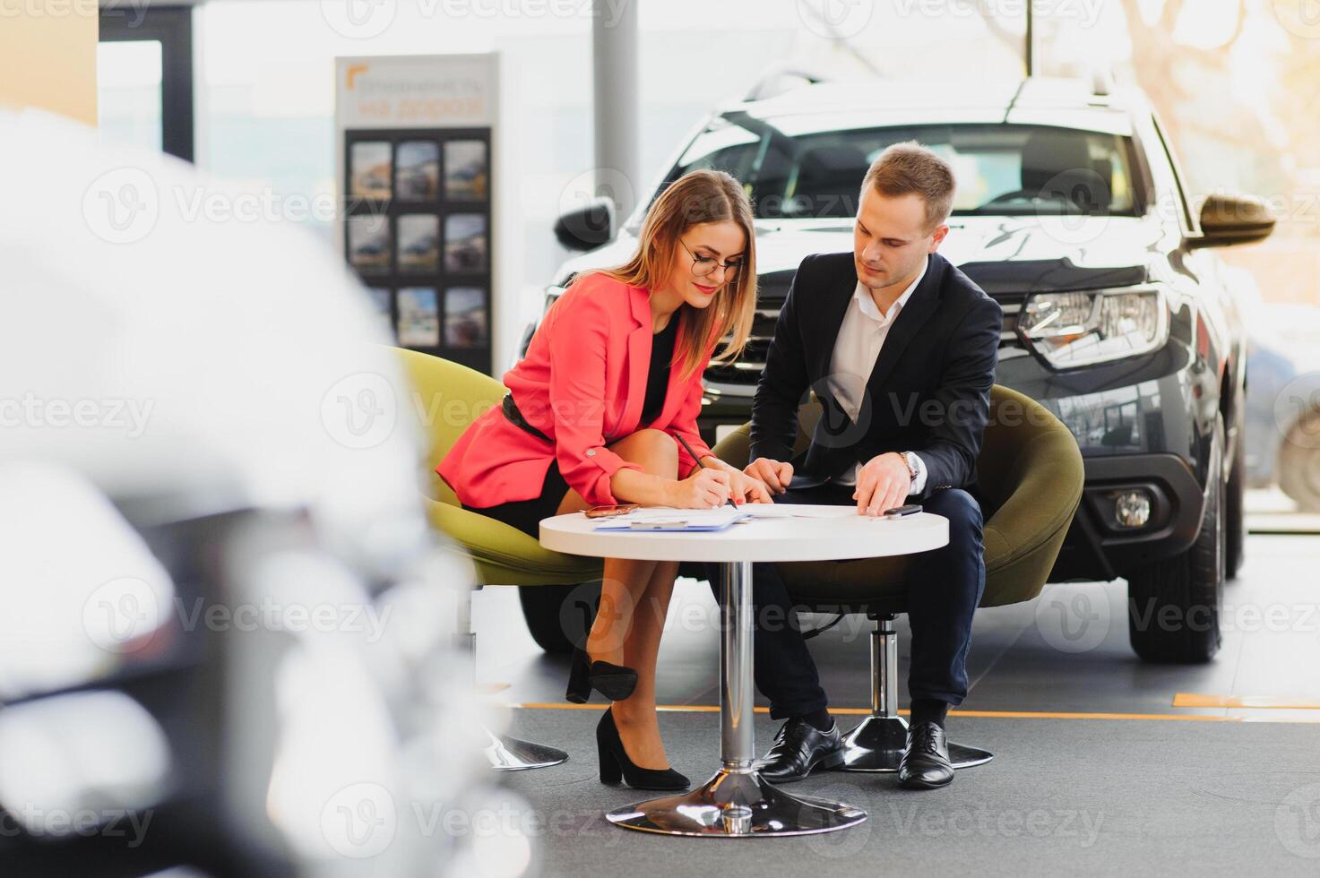 Car dealership sales person at work concept. Portrait of young sales representative wearing formal wear suit, showing vehicles at automobile exhibit center. Close up, copy space, background. photo