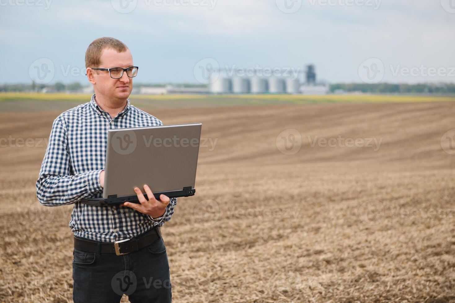 Harvesting concept. farmer in a field with a laptop on a background of a Agricultural Silos for storage and drying of grains, wheat photo