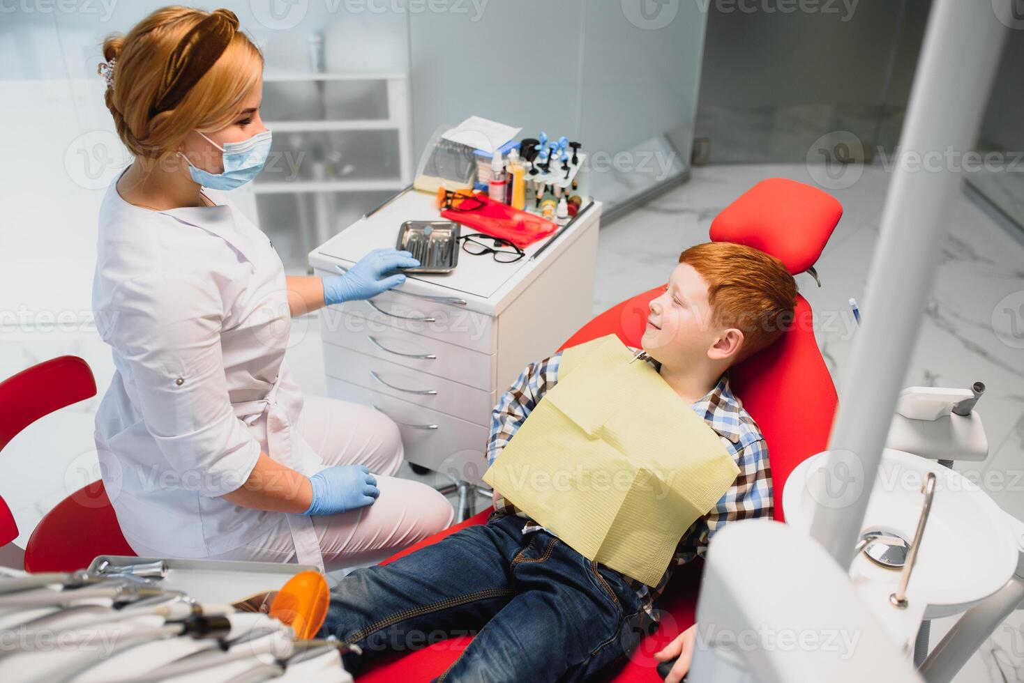 Dentist wearing mask. Red-haired child dentist wearing mask examining cute boy photo