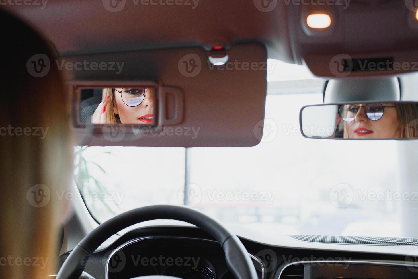 young woman looking in the rearview mirror of a car photo