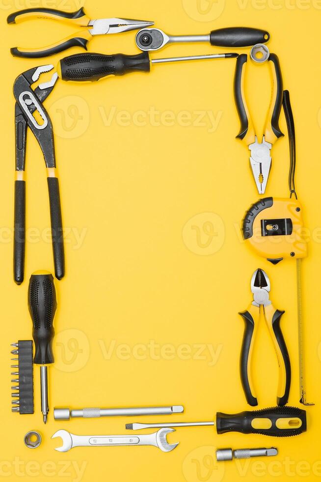 Tools top view on yellow background. Plier, open wrenches, screwdrivers and staple gun flat lay with copy space photo