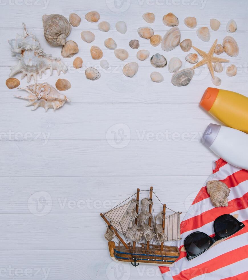 playa accesorios. toalla, chancletas, estrella de mar, barco y Gafas de sol en de madera antecedentes. parte superior ver con Copiar espacio. soleado tonificado foto