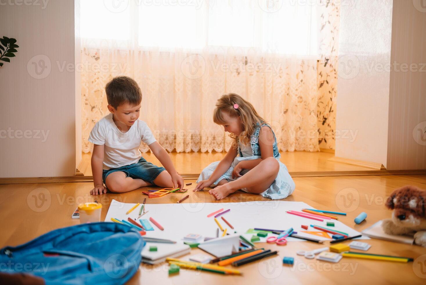 Kids drawing on floor on paper. Preschool boy and girl play on floor with educational toys - blocks, train, railroad, plane. Toys for preschool and kindergarten. Children at home or daycare photo