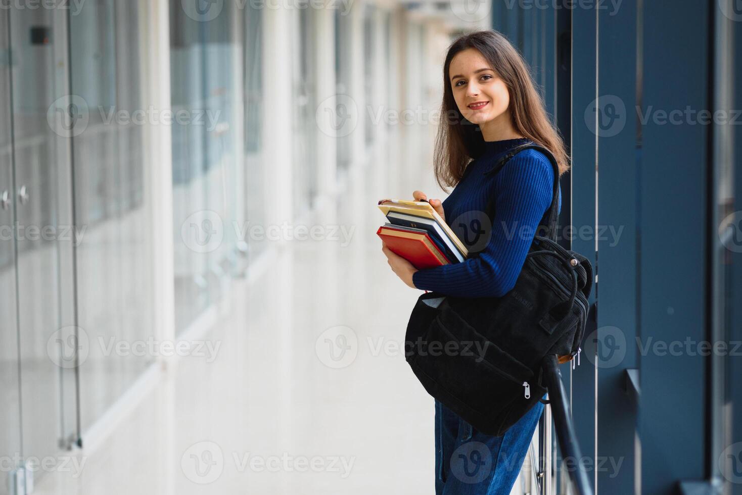Portrait of a pretty female student with books and a backpack in the university hallway photo