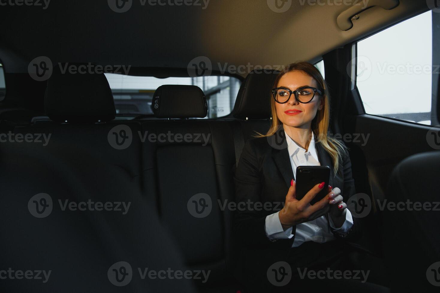 Some sort of interesting information. Smart businesswoman sits at backseat of the luxury car with black interior. photo