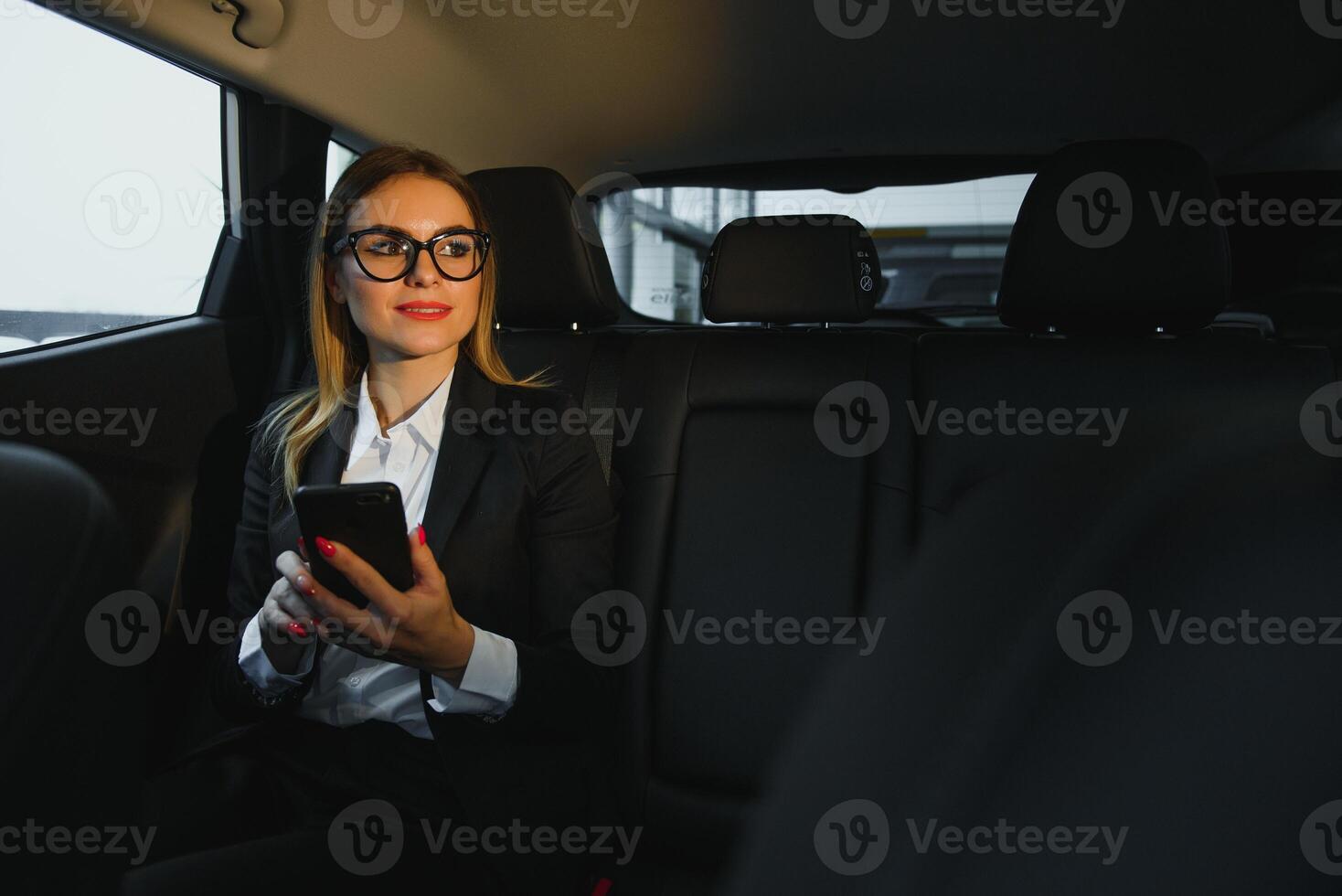 Some sort of interesting information. Smart businesswoman sits at backseat of the luxury car with black interior. photo