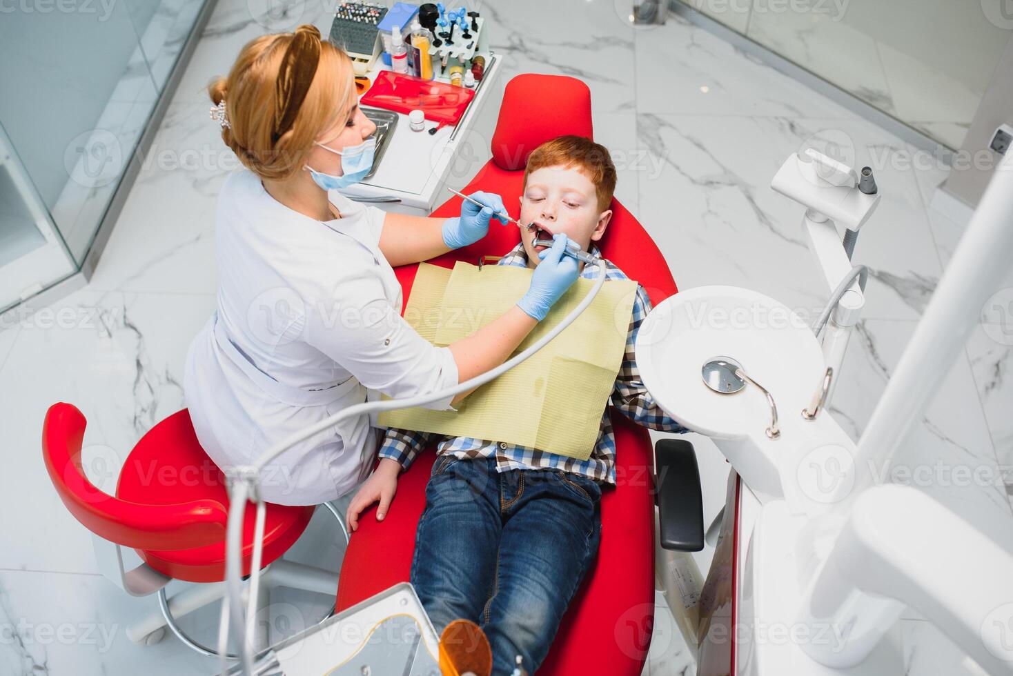 Pediatric dentist examining a little boys teeth in the dentists chair at the dental clinic photo