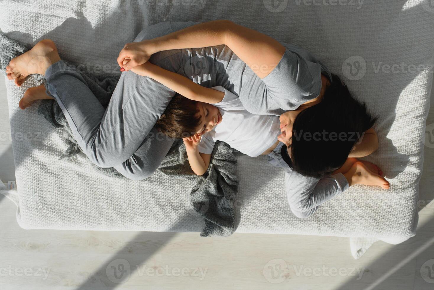 joven madre con su 4 4 años antiguo pequeño hijo vestido en pijama son relajante y jugando en el cama a el fin de semana juntos, perezoso mañana, calentar y acogedor escena. foto