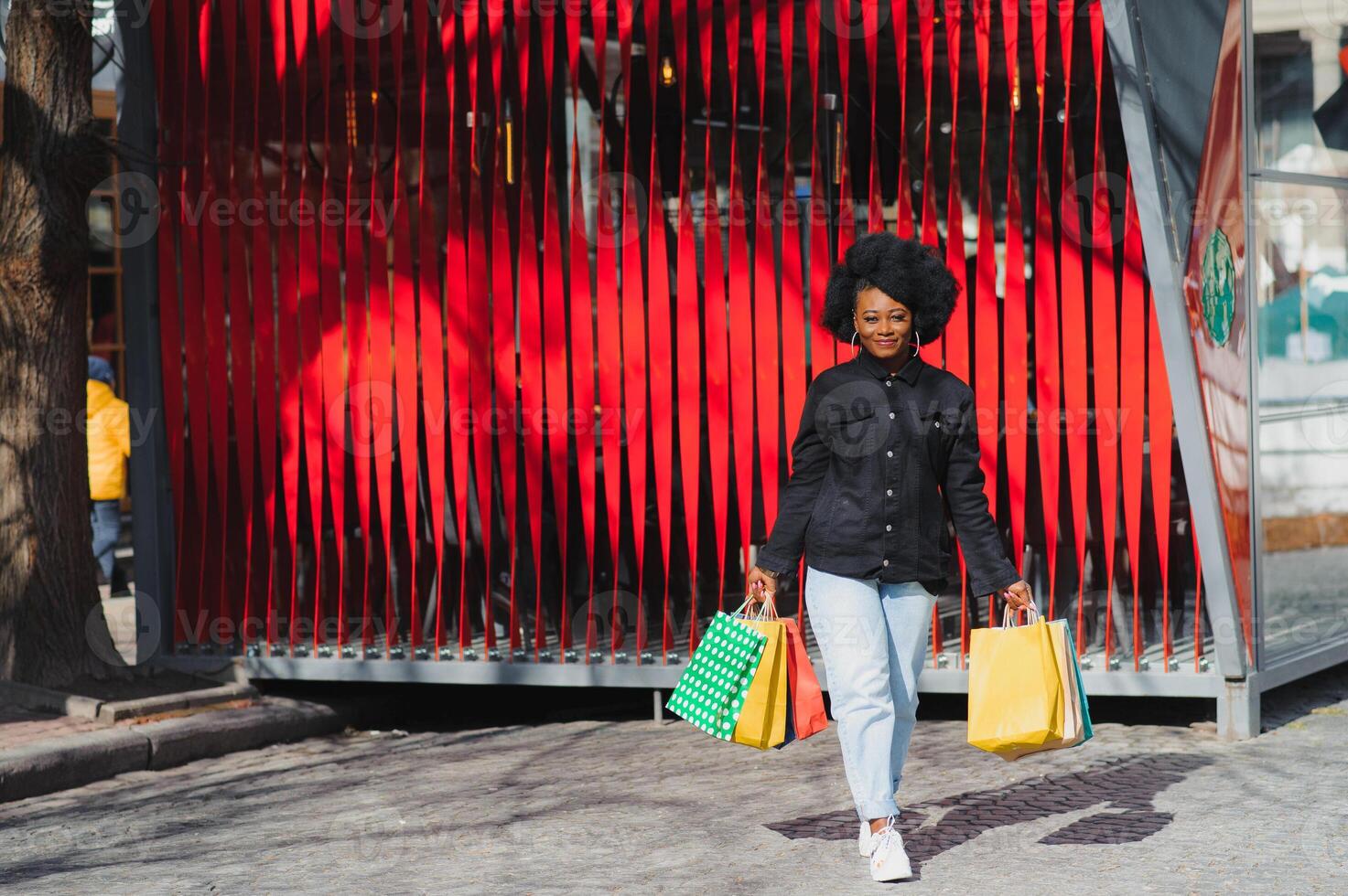 Portrait beautiful smiling african woman with shopping bags in city over red background photo