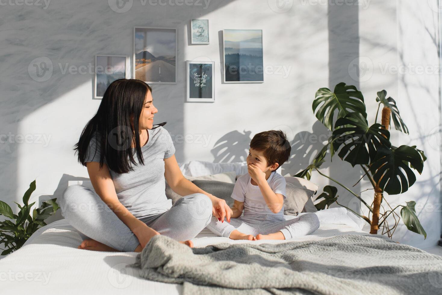 Beautiful pregnant woman and her cute little baby son are sitting in lotus position and smiling while meditating and doing yoga at home photo