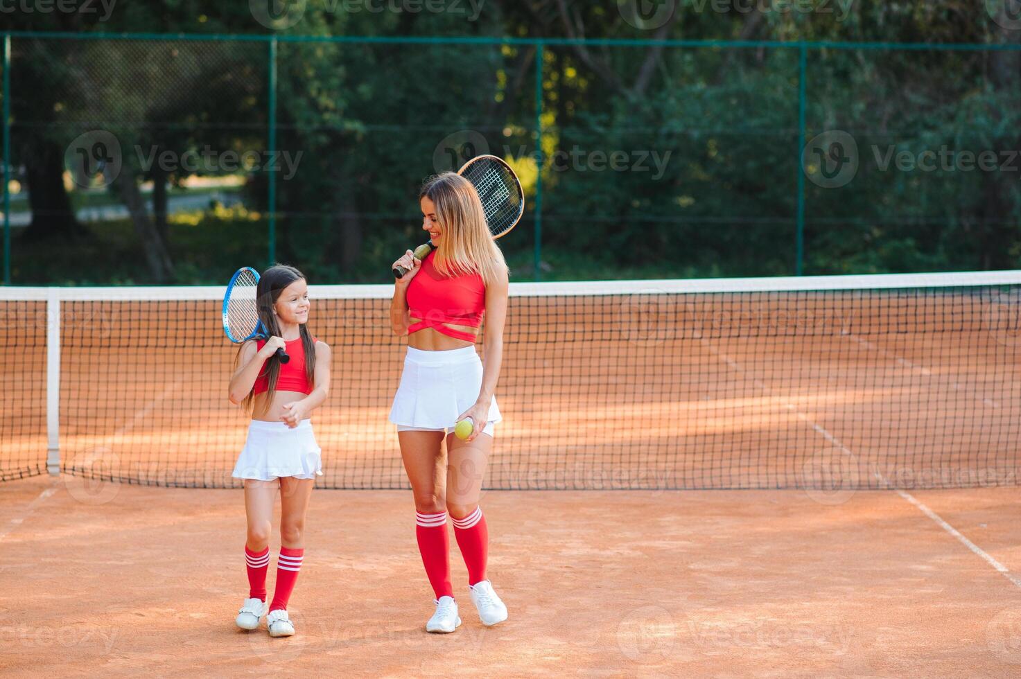 Little girl and her mother playing tennis on court photo