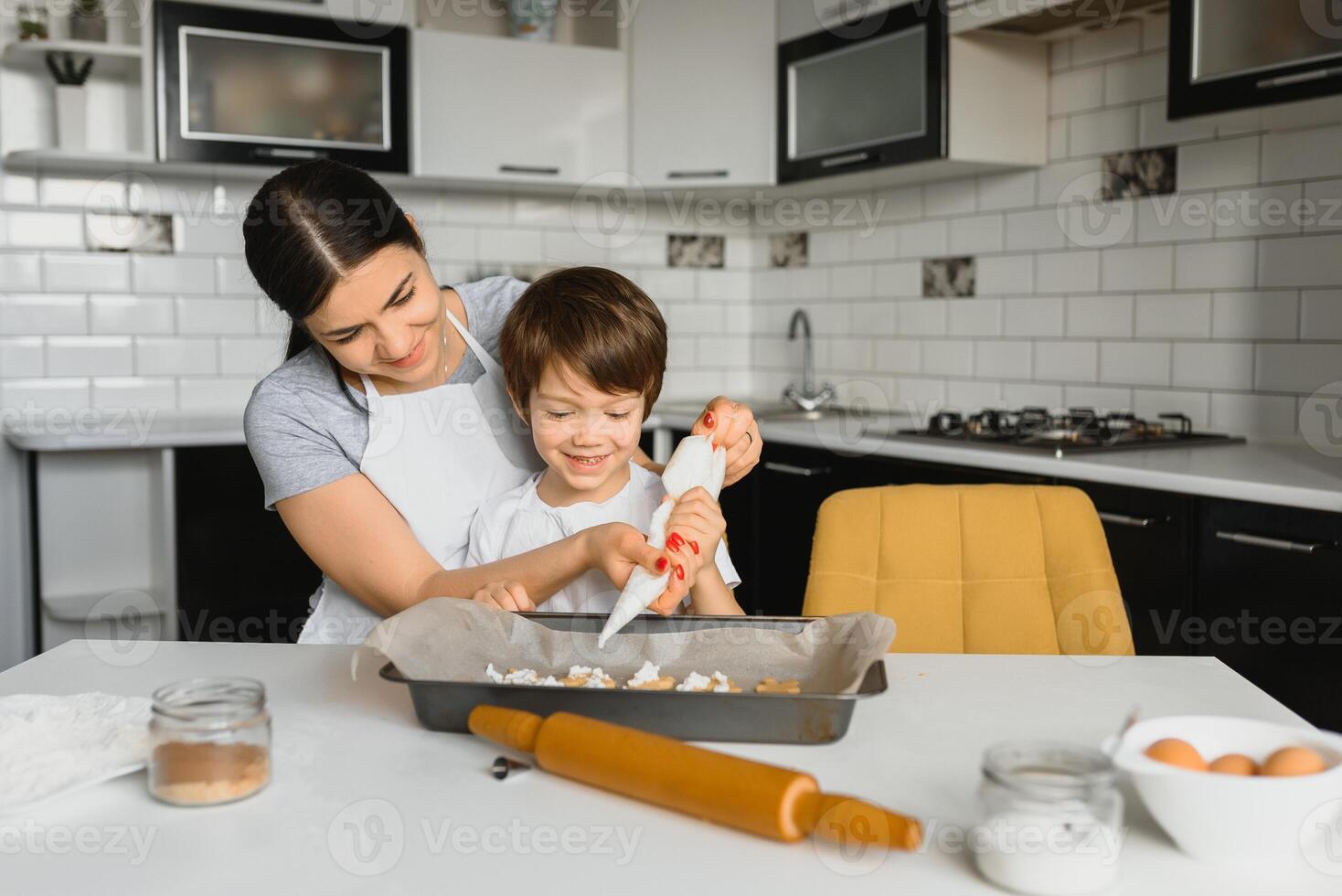 pequeño chico Ayudar su madre con el horneando en el cocina en pie a el mostrador junto a su amasadura el masa para el tarta foto