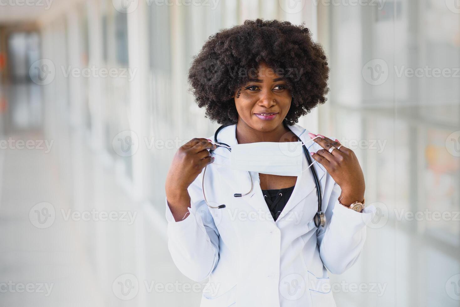 Closeup headshot portrait of friendly, smiling confident female healthcare professional with lab coat, arms crossed holding glasses. Isolated hospital clinic background. Time for an office visit photo