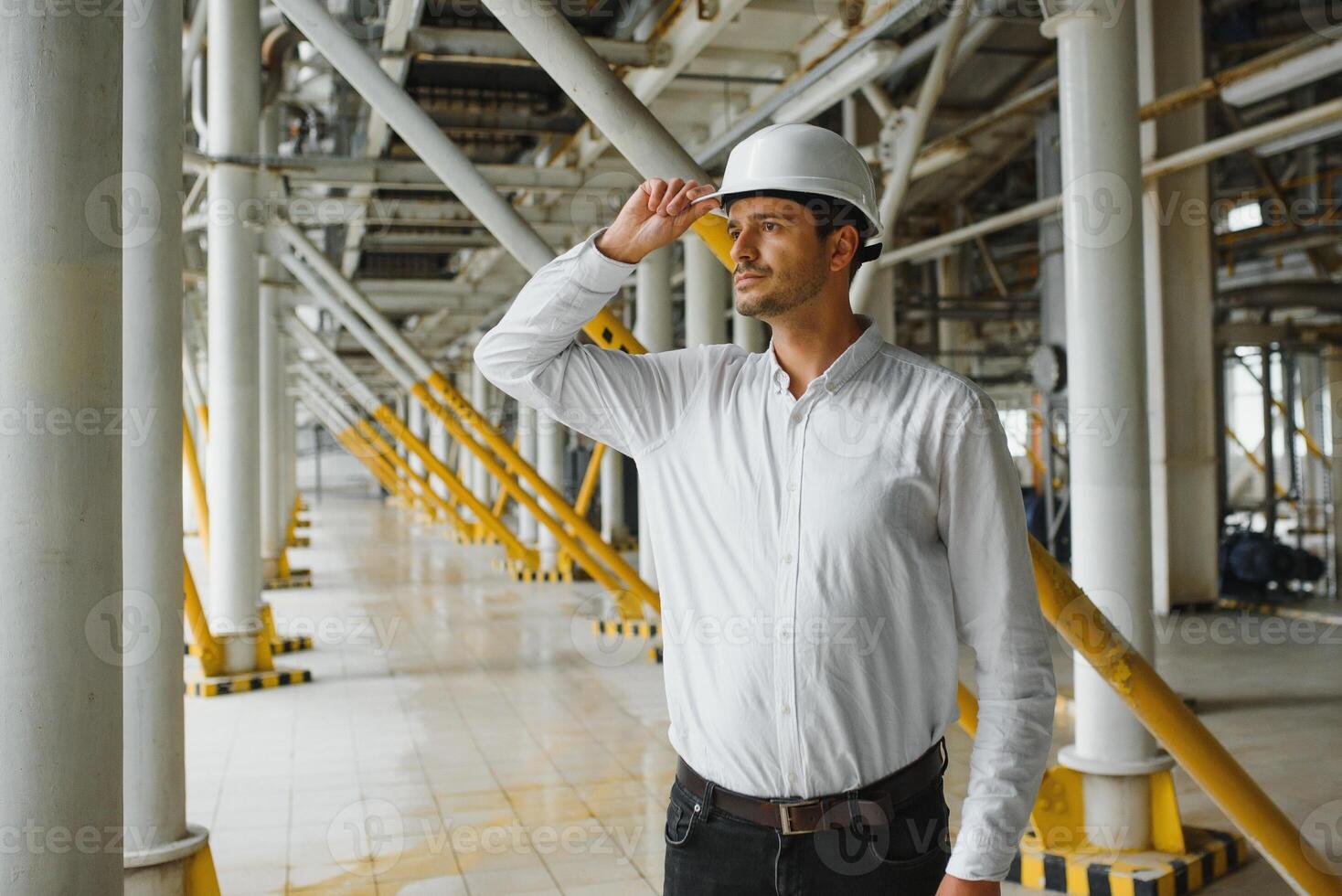 Smiling and happy employee. Industrial worker indoors in factory. Young technician with white hard hat. photo